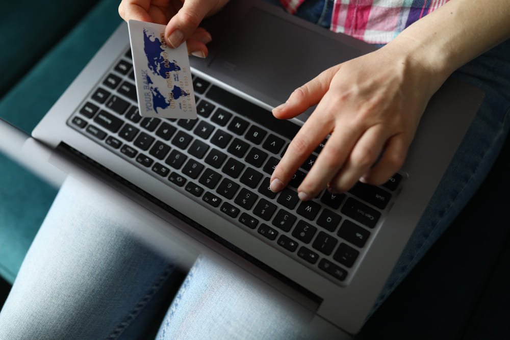 Kobieta trzyma laptop na kolanach i kartę kredytową w ręku